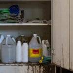 Rusted metal cabinet with doors open. Shelves are holding multiple containers of old pesticides.