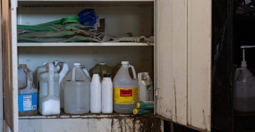 Rusted metal cabinet with doors open. Shelves are holding multiple containers of old pesticides.