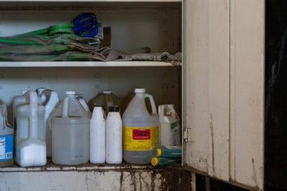 Rusted metal cabinet with doors open. Shelves are holding multiple containers of old pesticides.
