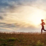 woman running on the field near seaside at sunset. Active person outdoors at the dusk in summer