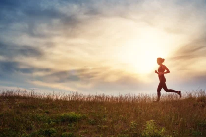 woman running on the field near seaside at sunset. Active person outdoors at the dusk in summer