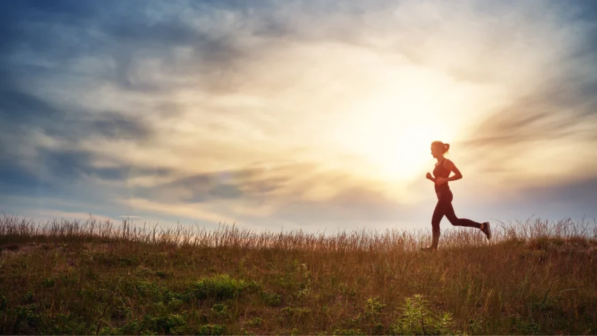 woman running on the field near seaside at sunset. Active person outdoors at the dusk in summer